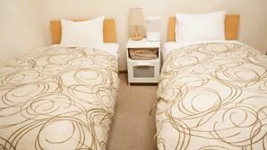 A hotel room with two single beds, a nightstand with a lamp and a device, and a small storage box.