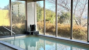 Una piscina interior con una estatua de piedra, ventanas amplias y vistas a árboles y arbustos.