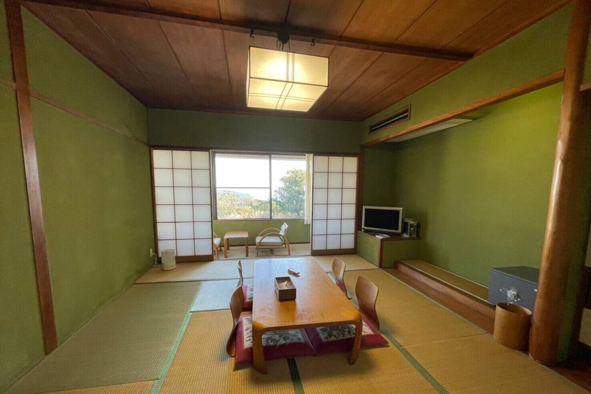 Um espaço com tatames, uma mesa baixa, cadeiras, uma televisão e portas deslizantes.