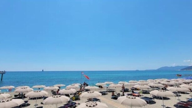 A beach with numerous umbrellas and a pier in the background. - Hostdomus - Bougainvillea House (Pietra Ligure)