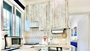 A kitchen with a microwave, a sink, and wooden cabinets. - Hostdomus - Bougainvillea House (Pietra Ligure)