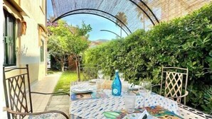An outdoor dining area with a table set for two, surrounded by chairs and a decorative umbrella. - Hostdomus - Bougainvillea House (Pietra Ligure)