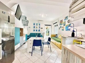 Un ambiente compatto con angolo cottura, zona pranzo e divano.