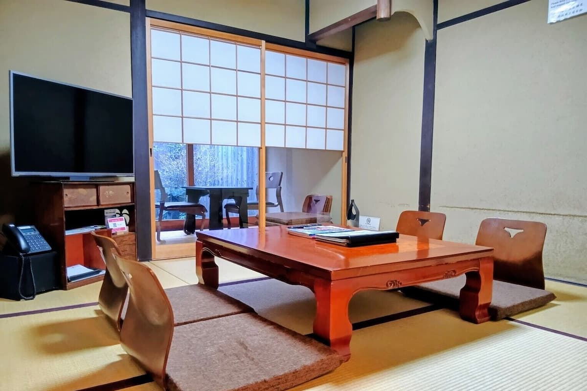 Ein traditioneller japanischer Raum mit Tatami-Böden, einem niedrigen Holztisch und einer Schiebetür mit Gittermuster.
