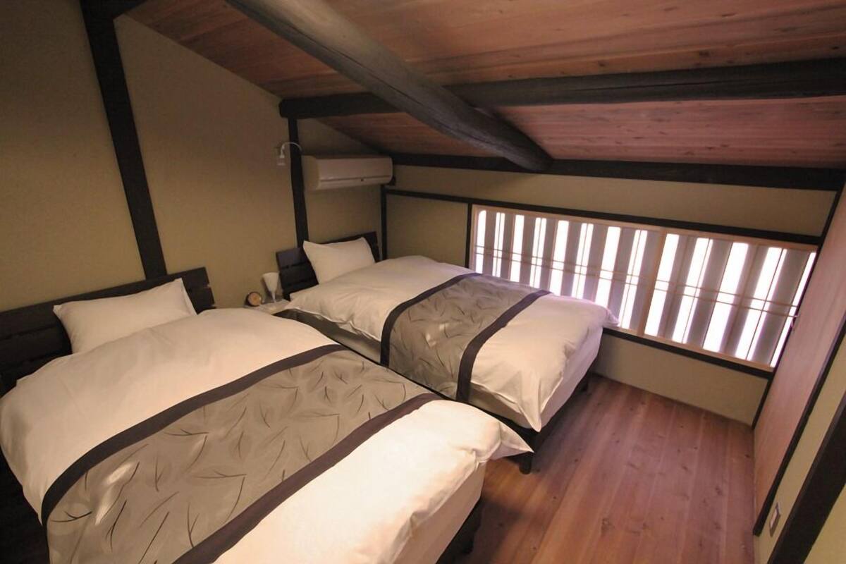 Ein Schlafzimmer mit zwei Betten, Holzboden, einem Fenster mit Jalousien und einer Klimaanlage.