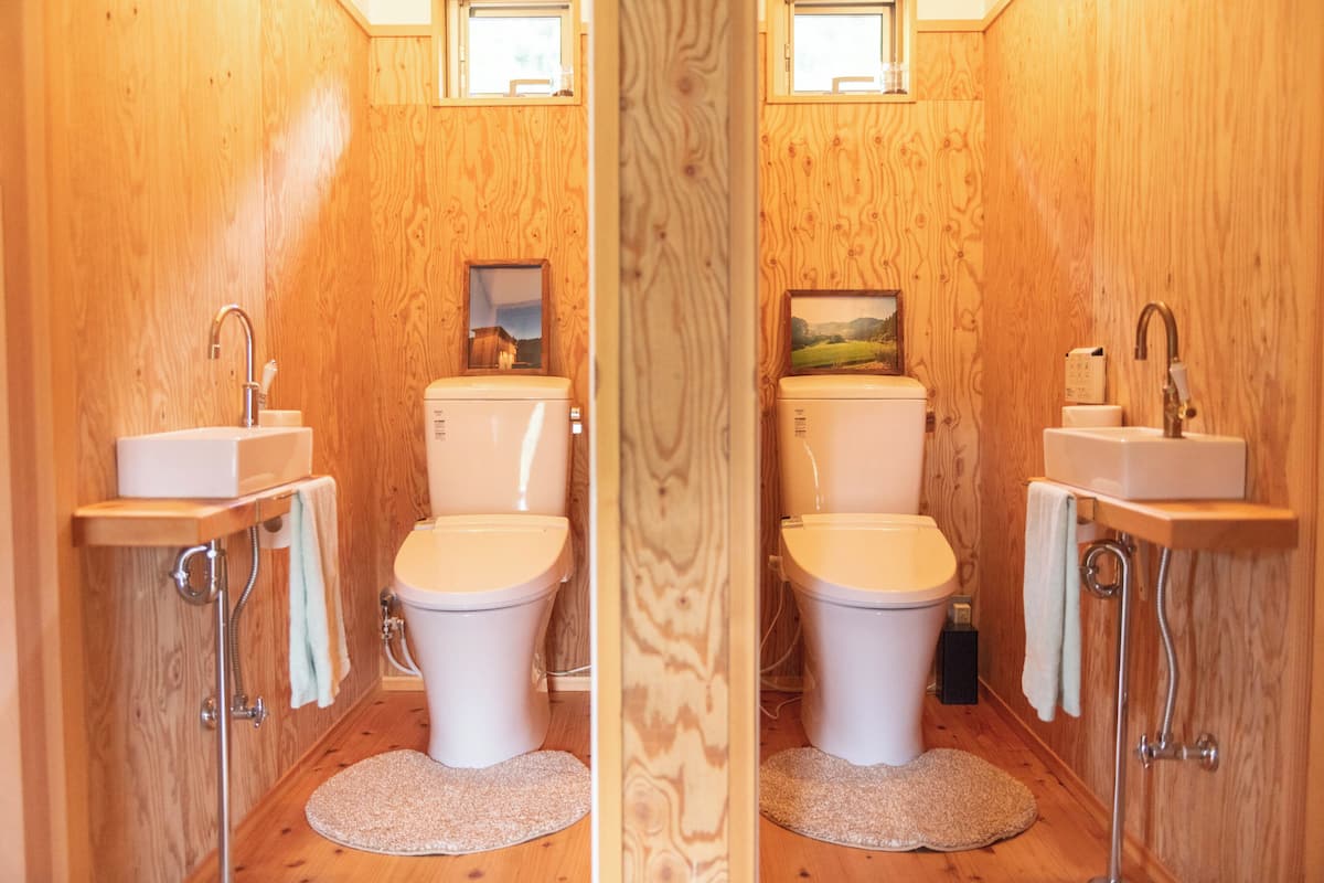 Une salle de bain aux murs lambrissés, équipée de deux toilettes, d’un lavabo et d’un miroir.
