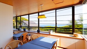 A room with a large window, wicker furniture, and a table with a blue tablecloth. - Izu Atagawa Onsen Yurakutei (Higashiizu)