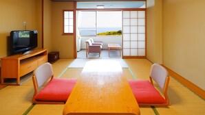 A traditional Japanese room with tatami flooring, a low table, two chairs, a television, and a sliding door leading to a balcony with a view. - Izu Atagawa Onsen Yurakutei (Higashiizu)