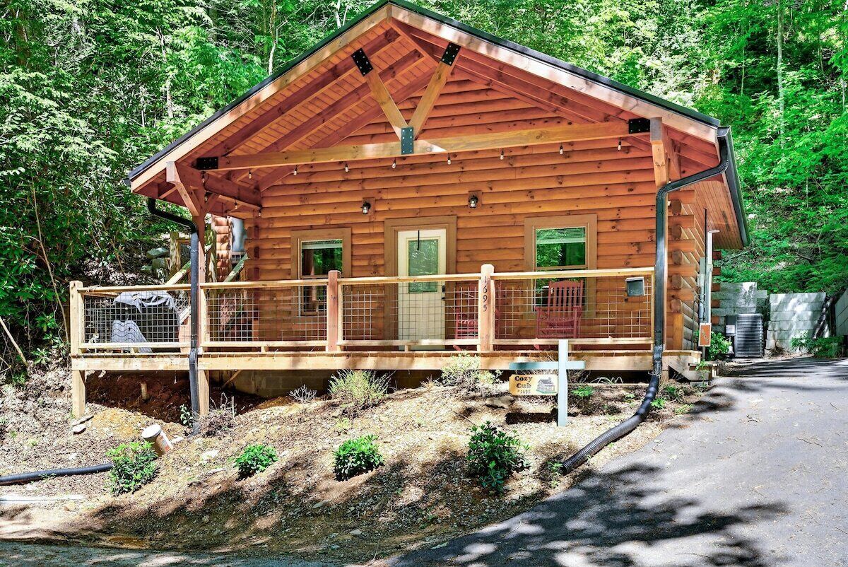 A wooden cabin with a fenced porch, surrounded by forest.