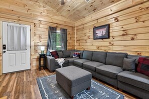 A cozy living room with a sectional sofa, a small ottoman, a side table with a lamp, and a framed picture on the wall. - Gatlinburg Cabin w/ Private Hot Tub & Free Tickets (Gatlinburg)