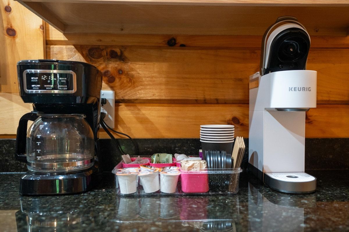 Une machine à café, une machine Keurig et un support à dosettes de café sont posés sur le plan de travail de la cuisine.