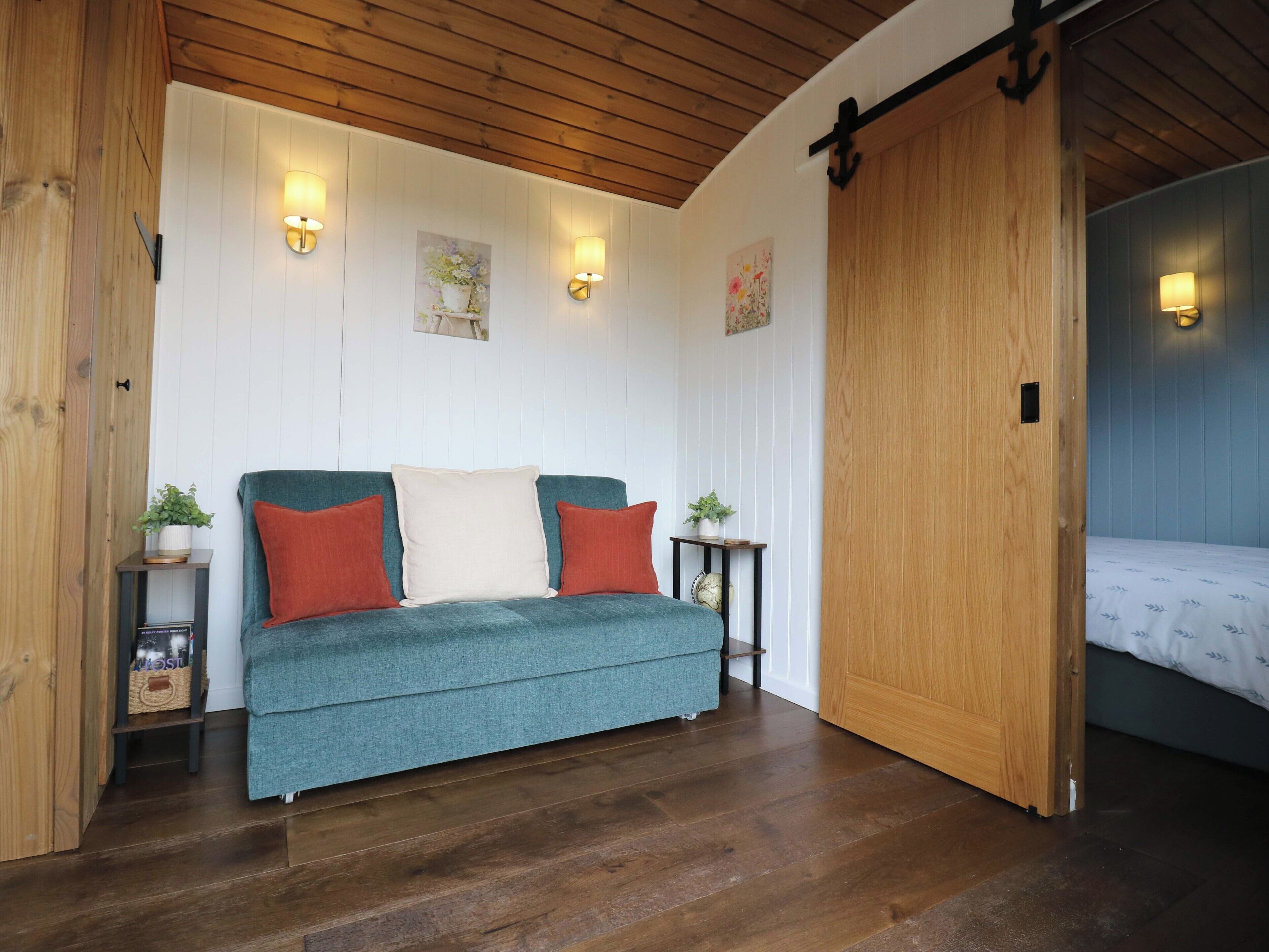 A cozy room with a teal sofa, wooden flooring, and a sliding door leading to another room.