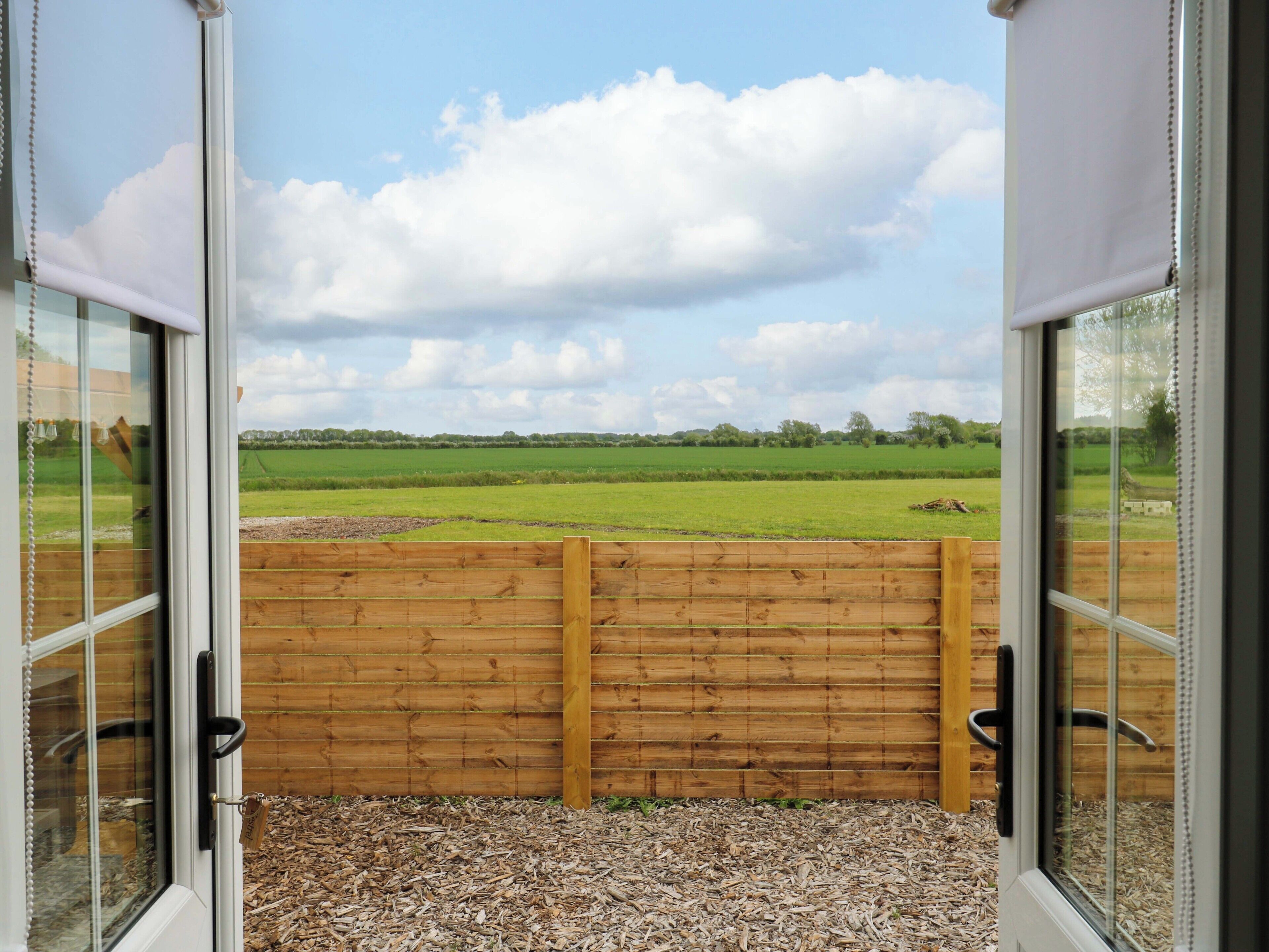 A view through a glass door with a wooden fence, leading to a green field and a cloudy sky.