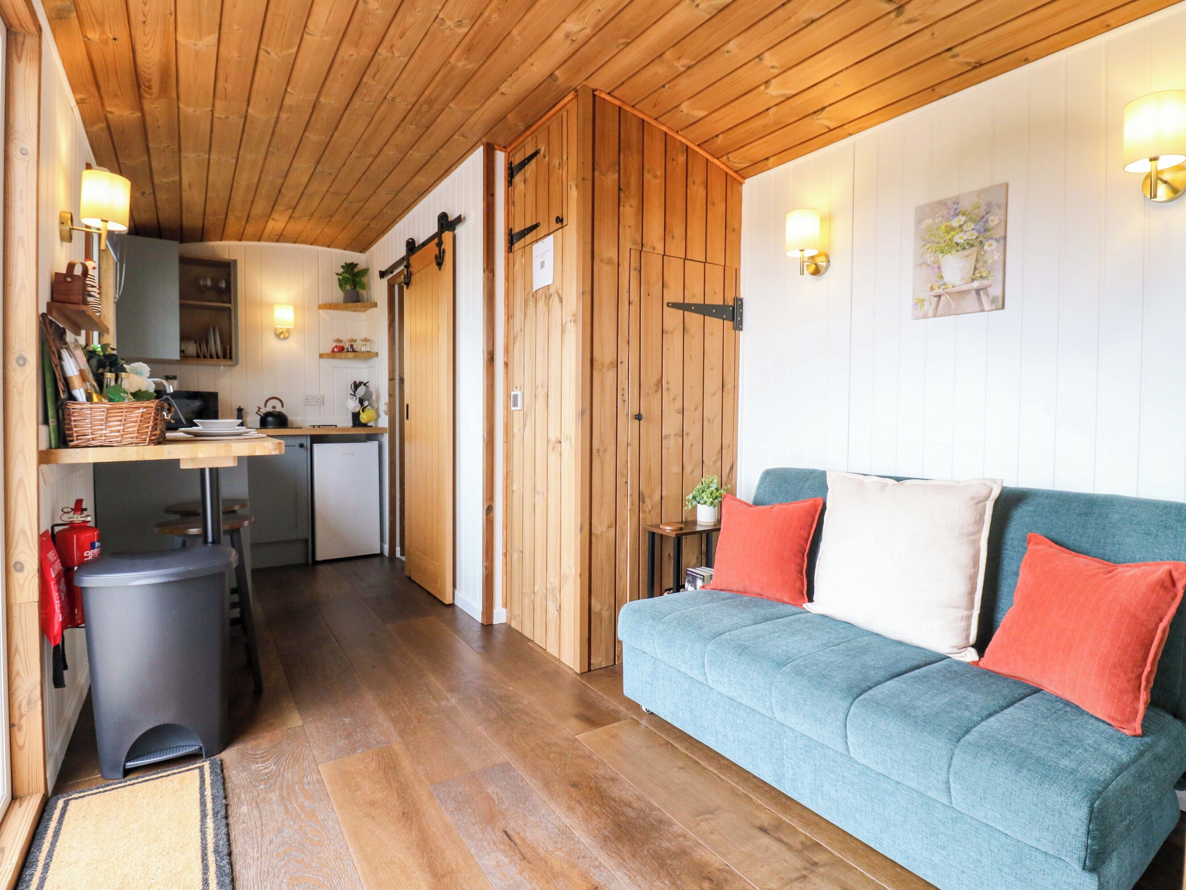 Una habitación acogedora con un sofá azul, techo de madera y una zona de cocina con un fregadero y armarios.