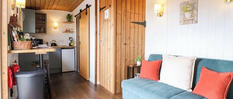 Una habitación acogedora con un sofá azul, techo de madera y una zona de cocina con un fregadero y armarios.