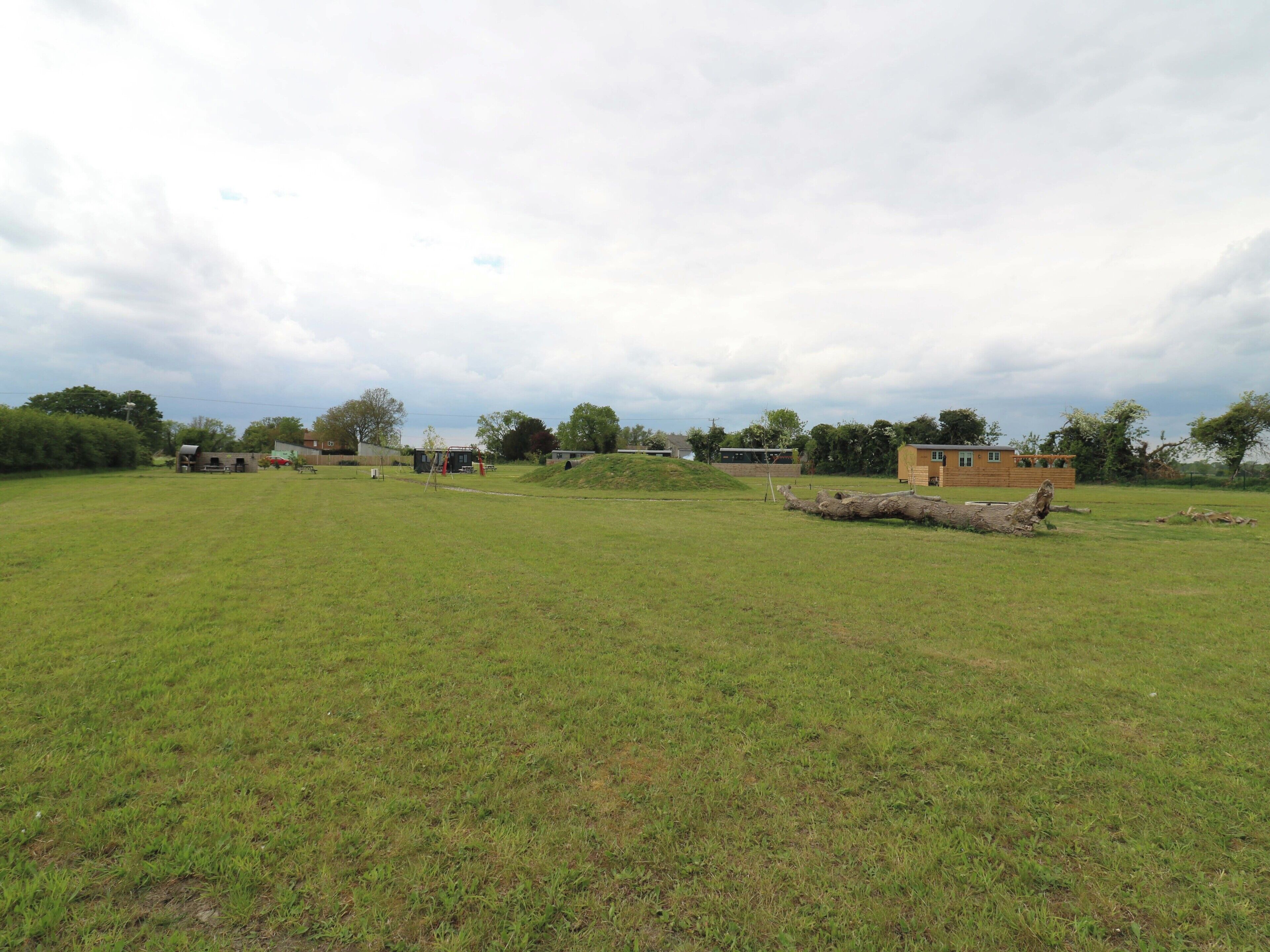 A grassy field with a small building and a large log.