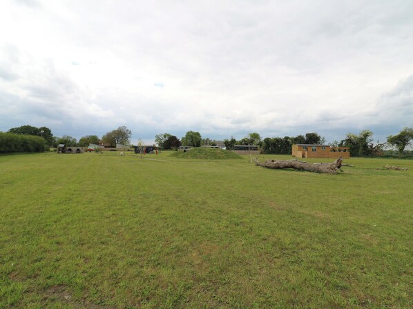 A grassy field with a small building and a large log. - The Kestrel (Cambridge)