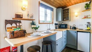 A kitchen with wooden cabinets, a microwave, a sink, and stools. - The Kestrel (Cambridge)