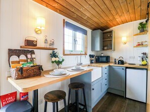 A kitchen with wooden cabinets, a microwave, a sink, and stools. - The Kestrel (Cambridge)