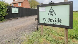 A sign for Lodeside Glamping with a tent and campfire symbol. - The Kestrel (Cambridge)