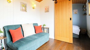 A cozy room with a teal sofa, wooden flooring, and a sliding door leading to another room. - The Kestrel (Cambridge)