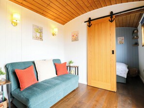 A cozy room with a teal sofa, wooden flooring, and a sliding door leading to another room. - The Kestrel (Cambridge)