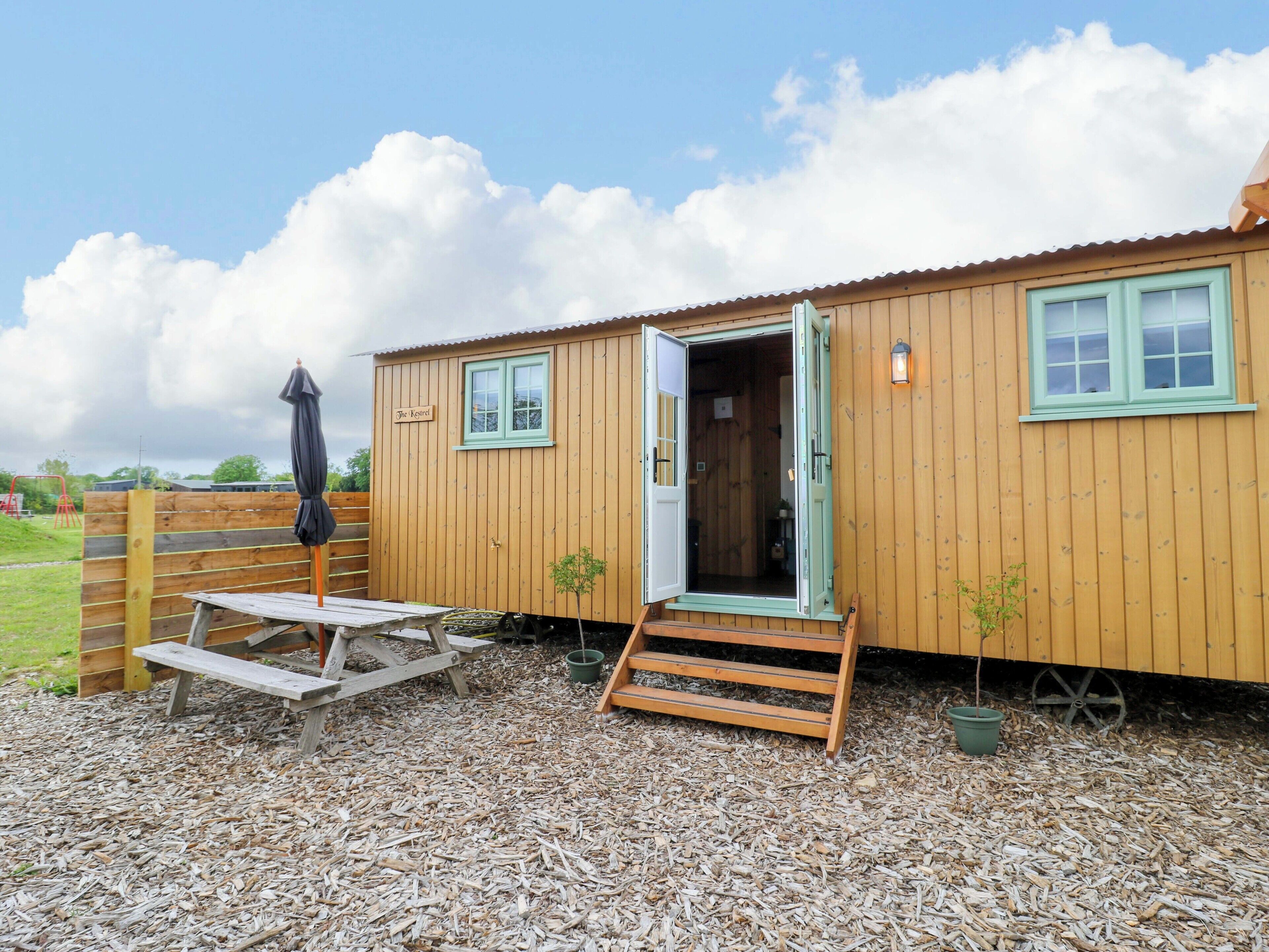 A wooden building with a door open, a small table, and a bench.