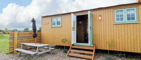 A wooden building with a door open, a small table, and a bench.