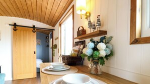 A wooden interior with a dining area featuring a table set with white plates and bowls, a vase with flowers, and a wall-mounted shelf with decorative items. - The Kestrel (Cambridge)