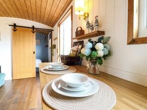 A wooden interior with a dining area featuring a table set with white plates and bowls, a vase with flowers, and a wall-mounted shelf with decorative items. - The Kestrel (Cambridge)