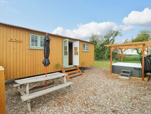 A wooden cabin with a sign reading 'The Kestrel,' a picnic table, a hot tub, and a pergola. - The Kestrel (Cambridge)