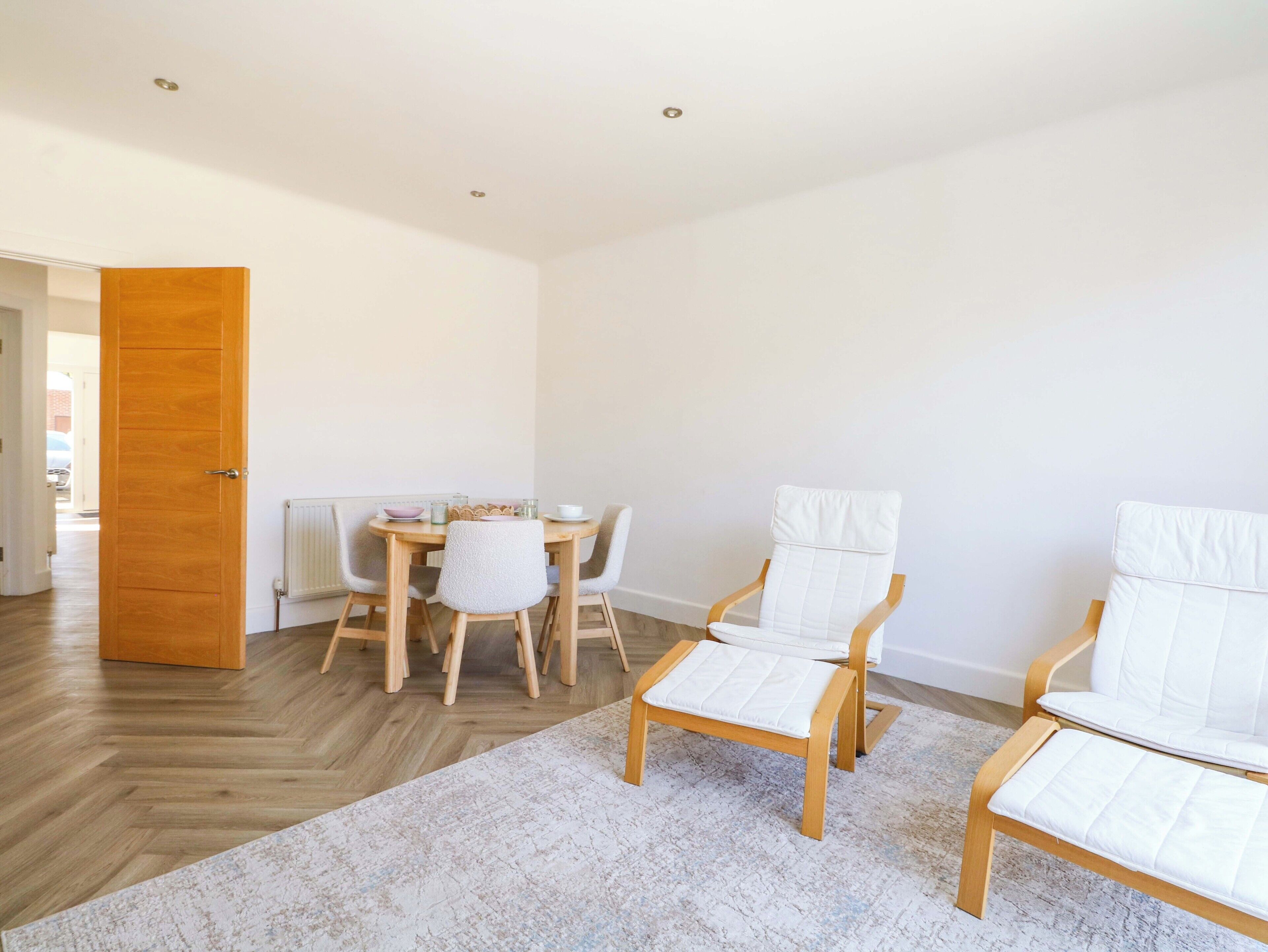 A modern dining area with a wooden table, white chairs, and a patterned rug.