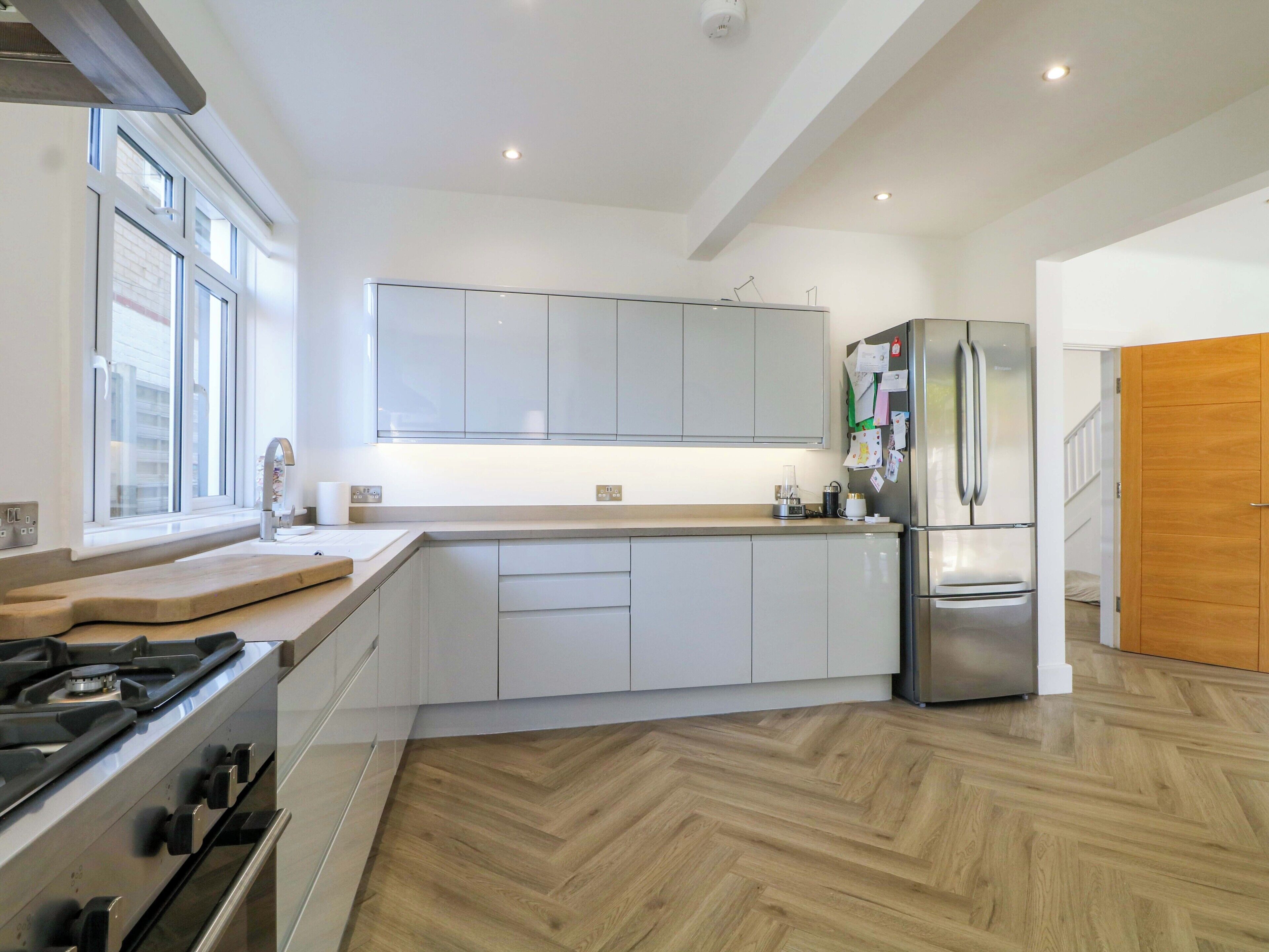 A modern kitchen with white cabinetry, a stainless steel refrigerator, and a herringbone-patterned wooden floor.