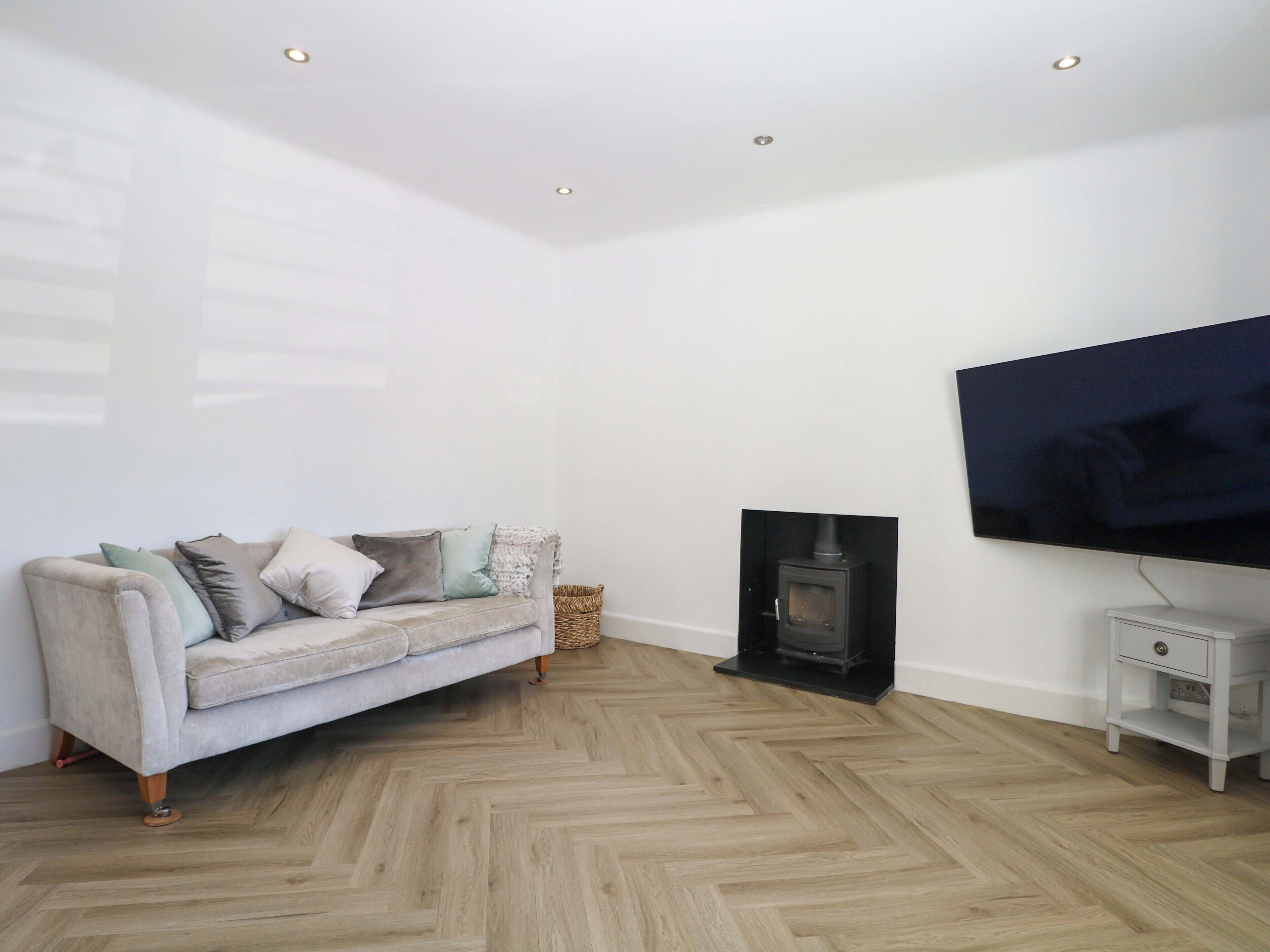 A living room with a sofa, a television, a fireplace, and a herringbone-patterned floor.