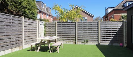 A backyard with a wooden fence, a picnic table, and artificial grass.
