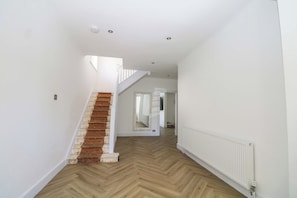 Ein Flur mit einer Holztreppe, weißen Wänden und einem Heizkörper.
