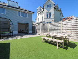 Ein Garten mit künstlichem Rasen, einer Holzbank, einem Tisch und einem Gartenstuhl.