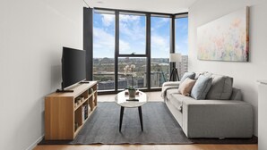 A modern living room with a large window, a flat-screen TV, a grey sofa, and a coffee table. - Melbourne Square Southbank (Southbank)