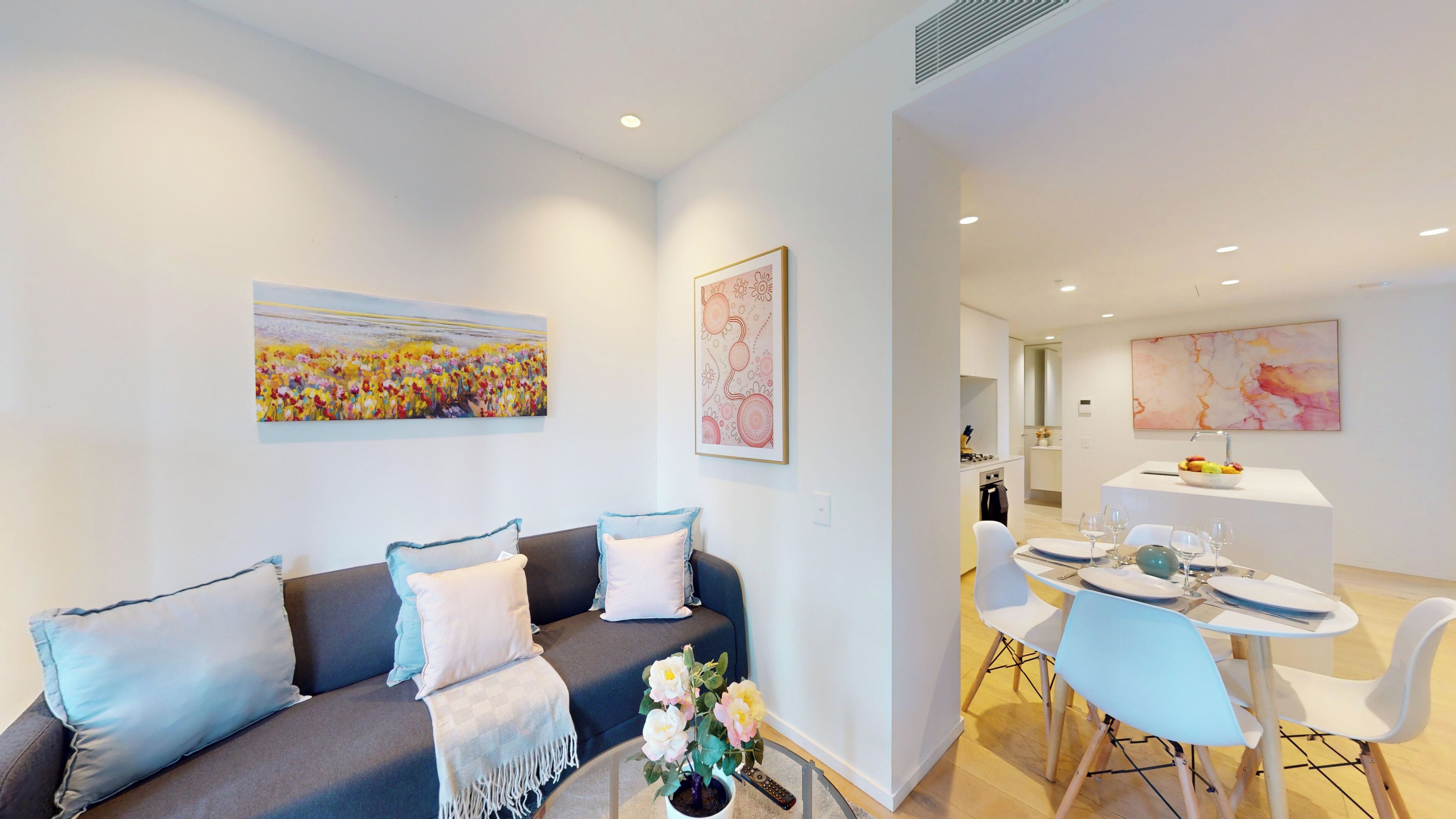 A modern living room with a sofa, a dining area with a table and chairs, and a kitchen in the background.