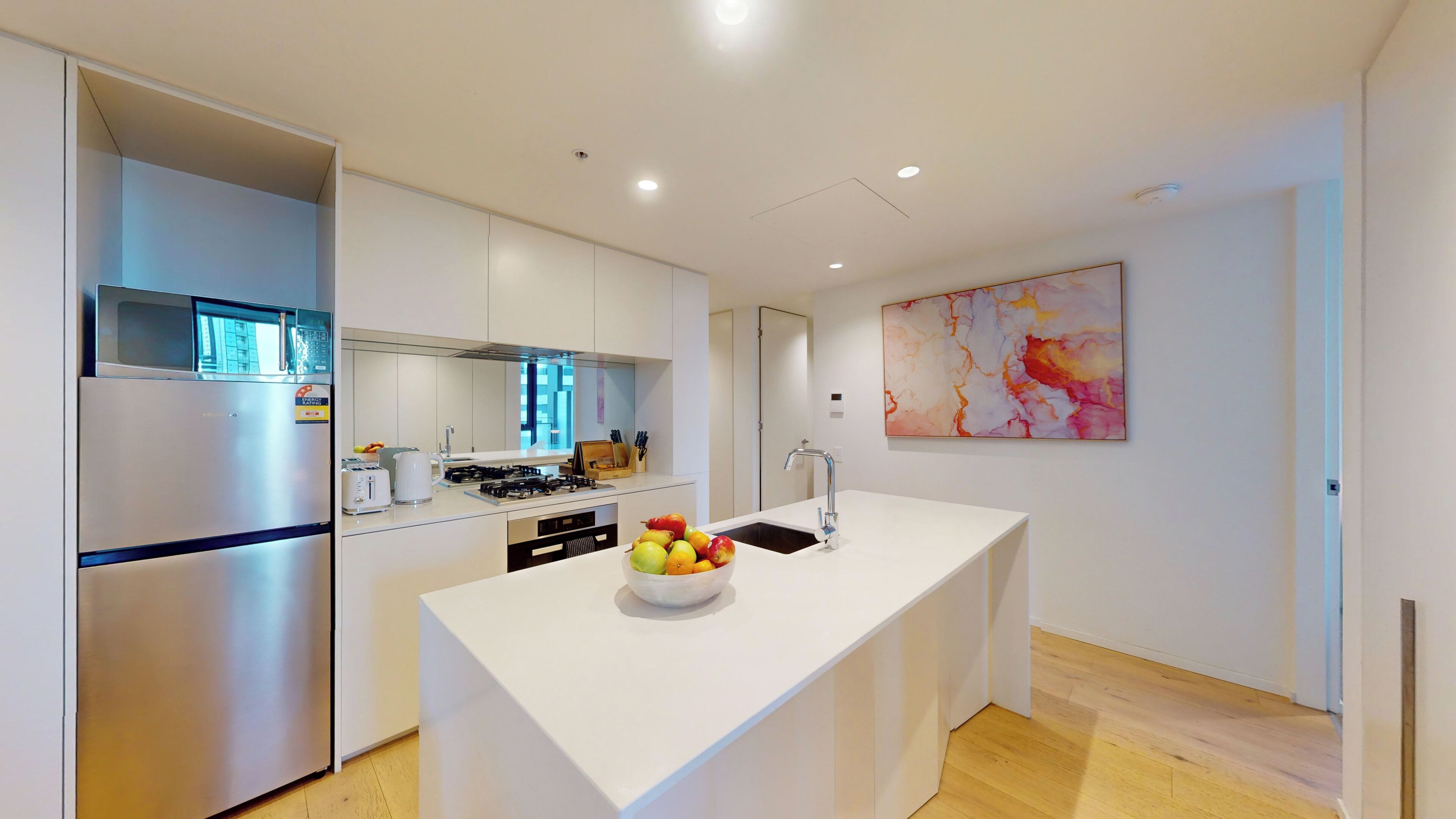 Una cocina moderna con una isla central, electrodomésticos de acero inoxidable y un frutero.