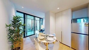 A modern kitchen with a built-in microwave, a dining table set for four, and a large window offering a view of the city. - Melbourne Square Southbank (Southbank)