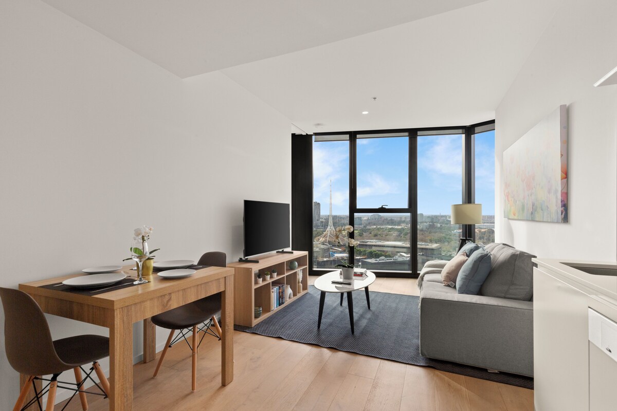 A modern living room with a dining area, a sofa, a TV, and a large window with a city view.