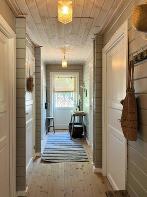 A hallway with wooden floors, a door with a window, a hanging light fixture, and a basket on the floor. - Summer house with soul and family roots in Rørvig (Nykøbing Sjælland)