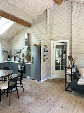 A kitchen with a refrigerator, stove, and dining area with chairs. - Summer house with soul and family roots in Rørvig (Nykøbing Sjælland)