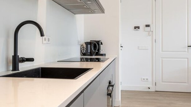 A modern kitchen with a black faucet, a stainless steel range hood, and a black coffee machine. - Bright Ground-floor Apartment With Garden (Rotterdam)
