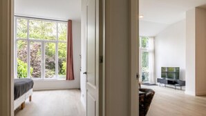 A room with a bed, a TV, and a large window. - Bright Ground-floor Apartment With Garden (Rotterdam)