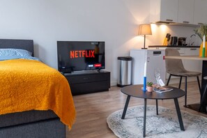A modern hotel room with a bed, a TV displaying 'NETFLIX,' a small table with a lamp, and a kitchenette area. - Prachtige Studio in Hartje Rotterdam (Rotterdam)