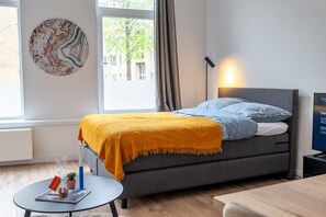 A modern bedroom with a bed, a small table, a lamp, and a wall art piece. - Prachtige Studio in Hartje Rotterdam (Rotterdam)
