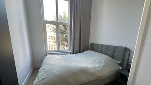 Quarto com uma cama de solteiro, janela com cortinas e radiador.