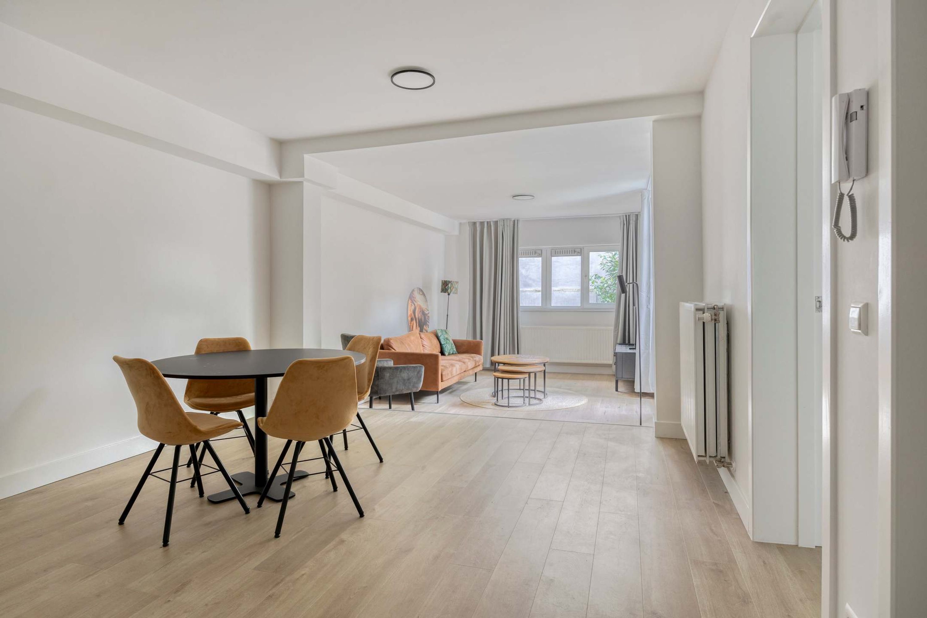 A modern living room with a dining area, a sofa, and a view of the outside.